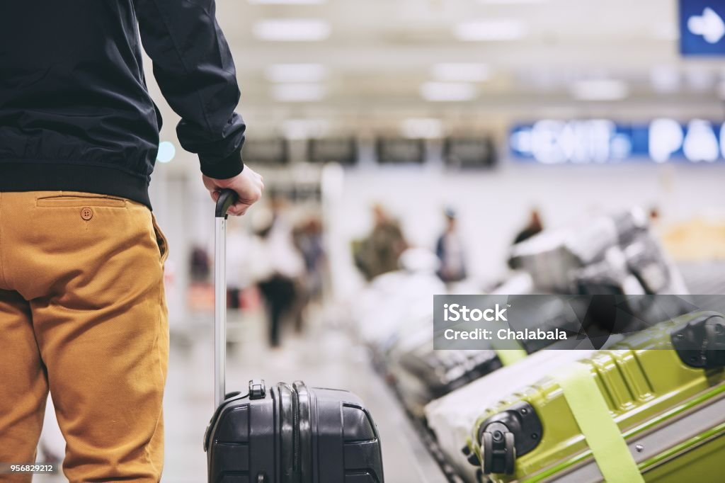 Man in airport terminal Man traveling by airplane. Young passenger holding his suitcase near baggage claim in airport terminal. Airport Stock Photo