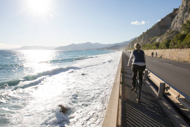 Woman biking along Mediterranean Sea at sunrise She is biking on an elevated pathway above the sea and along the aurelia, Borgio Verezzi, Liguria finale ligure stock pictures, royalty-free photos & images