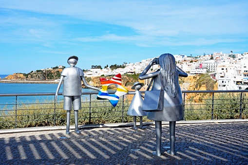 Metal sculpture of a woman taking a photo of her husband and daughter at the Miradouro do Pau da Bandeira with views of the town and ocean to the rear, Albufeira, Portugal, Europe.