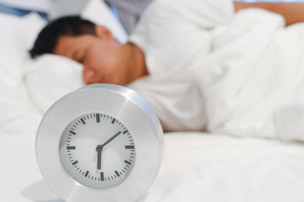 istock Alarm clock waking up at morning with a man sleeping on bed. 956861712