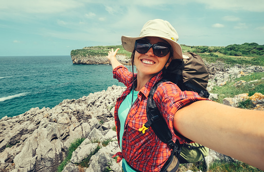 Viajero mochilero de mujer feliz fotografiar selfie en la impresionante costa del océano photo