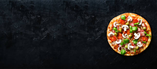 istock Fresh italian pizza with mushrooms, ham, tomatoes, cheese, olive, basil on black concrete background. Copy space. Homemade with love. Fast delivery. Recipe and menu. Banner 956865098