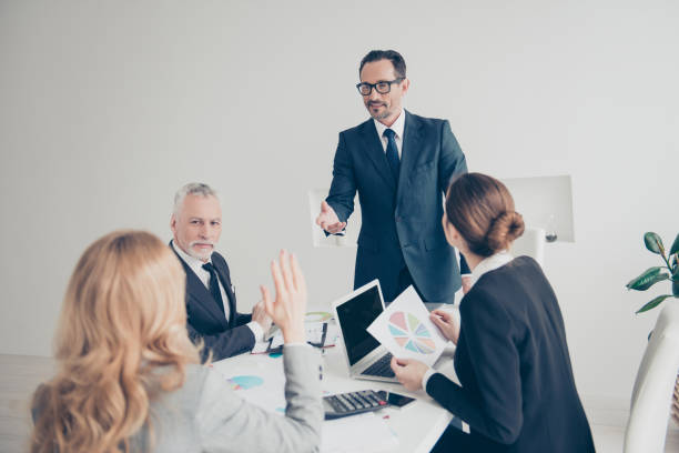 istock Portrait of financial, attractive, stylish expert in suits making training, asking agents questions, blonde woman raised her hand want to answer, sitting in workplace, workstation at desk 956870104