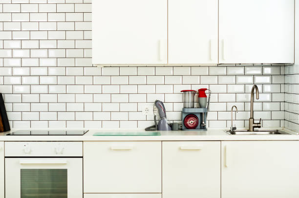 istock White minimalistic kitchen interior and design. Tile wall background. Household appliances - blender, vacuum machine, modern stove, dishwasher, oven, table, faucet mixer 956874048