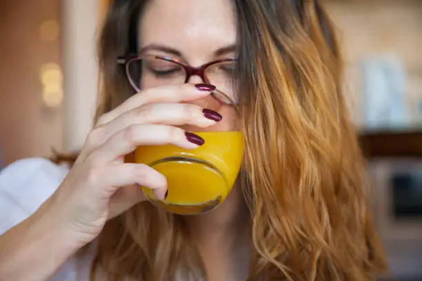 Close-up shot of a young woman drinking refreshing juice in the morning.