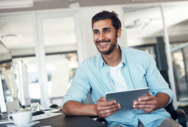 He's got big designs for the future of his business Shot of a young businessman using a digital tablet in a modern office business man looking away stock pictures, royalty-free photos & images