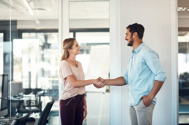 Teaming up to take their business places Shot of a businessman and businesswoman shaking hands in a modern office casual handshake stock pictures, royalty-free photos & images