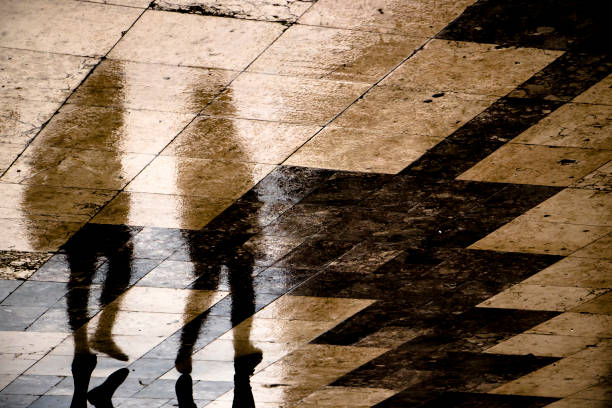 istock Blurry reflection silhouette of two people walking together in the rain 956885964