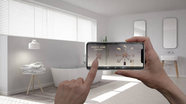 istock Remote home control system on a digital smart phone tablet. Device with app icons. Interior of minimalist white bathroom in the background, architecture design. 956891858