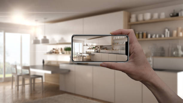 istock Hand holding smart phone, AR application, simulate furniture and interior design products in real home, architect designer concept, blur background, modern kitchen 956895012
