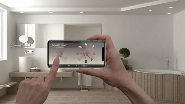 istock Remote home control system on a digital smart phone tablet. Device with app icons. Interior of minimalist white bathroom in the background, architecture design. 956895278