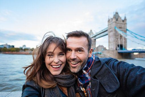 Happy couple making selfie with Tower Bridge in the background. Autumn season.