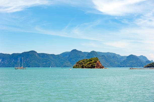 Schooner yacht and small boat in a wooded bay of the Langkawi archipelago of 99 islands on Malaysia's west coast, seen from Langkawi island with calm sea, Kedah, Malaysia
