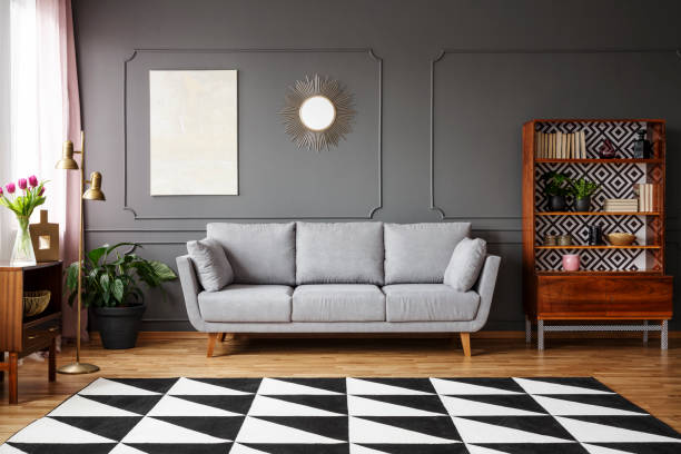 istock Black and white carpet with geometric pattern placed on the floor in dark living room interior with grey couch, vintage cupboard with books and wainscoting on the wall 956907326