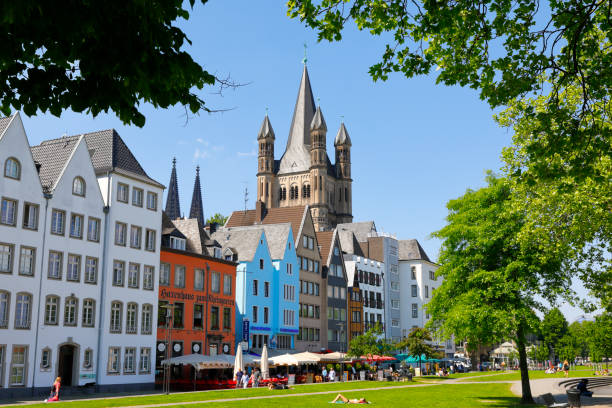 Cologne, Germany - May 08, 2018. The historic old town district with a row of medieval buildings and the Great Saint Martin Church in the centre. The two towers of the Cologne Cathedral in the background. A lot of tourists enjoy the sunny spring afternoon.