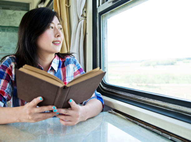 istock Young asian woman reading book on a train 956924720