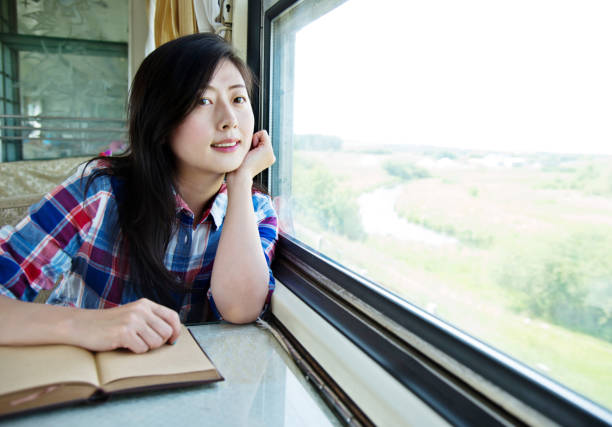 istock Young asian woman reading book on a train 956925280