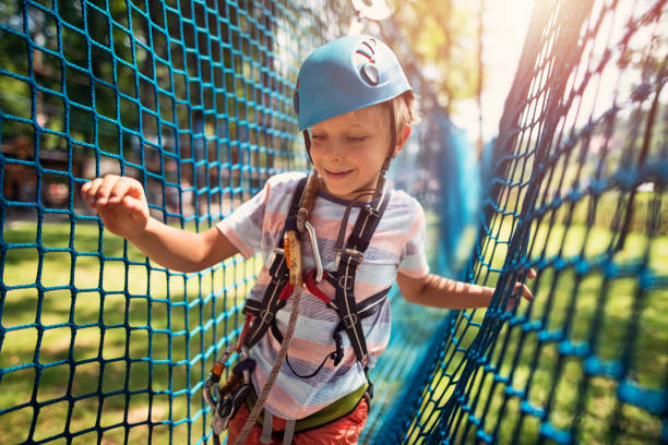 Little boy in outdoors adventure park. The boy aged 7 is smiling and walking in a safety net obstacle.\nNikon D800