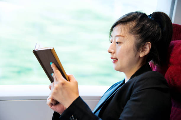 istock Young woman reading book on a train 956931306