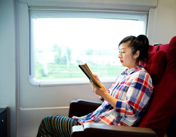 istock Young woman reading book on a train 956931550