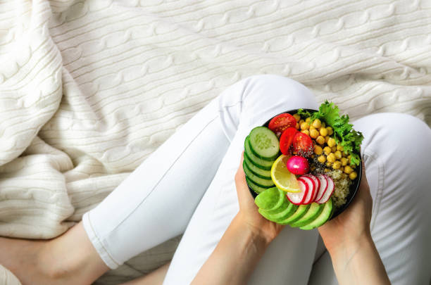 Girl in white jeans holds in hands fork, vegan breakfast meal in bowl with avocado, quinoa, cucumber, radish, salad, lemon, cherry tomatoes, chickpea, chia seeds. Top view, copy space. Clean eating. chica en jeans blanco posee en la bifurcación de manos, comida de desayuno vegano en tazón de fuente con palta, quinoa, pepino, rábano, ensalada, limón, tomates cherry, garbanzos, semillas de chia. vista superior, con copia espacio. limpiar comer