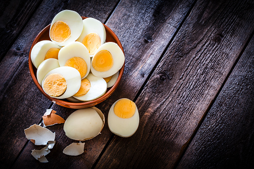 Top view of a brown clay bowl filled with hard-boiled eggs halves shot on rustic wooden table. The composition is at the left of an horizontal frame leaving useful copy space for text and/or logo at the right. Low key DSRL studio photo taken with Canon EOS 5D Mk II and Canon EF 100mm f/2.8L Macro IS USM