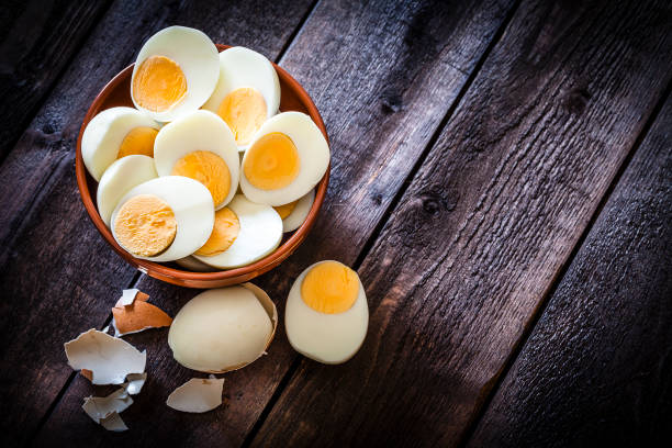 Hard-boiled eggs Top view of a brown clay bowl filled with hard-boiled eggs halves shot on rustic wooden table. The composition is at the left of an horizontal frame leaving useful copy space for text and/or logo at the right. Low key DSRL studio photo taken with Canon EOS 5D Mk II and Canon EF 100mm f/2.8L Macro IS USM boiled egg photos stock pictures, royalty-free photos & images