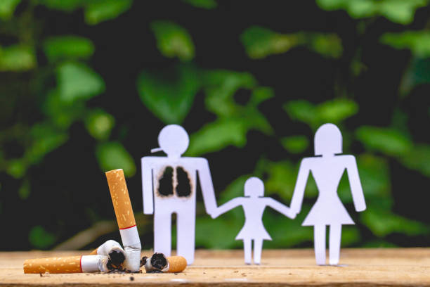 Paper dolls, parents and daughter. Daddy doll have burned lungs. Their hands hold hands with their daughter. There are burned cigarettes butts. stock photo