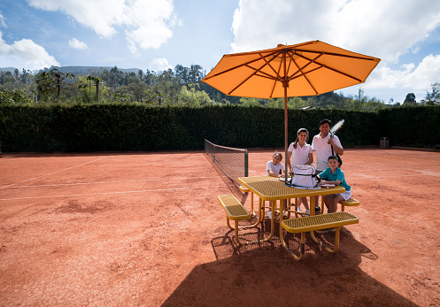 Portrait of family sitting on table at the tennis court looking at camera smiling very happy