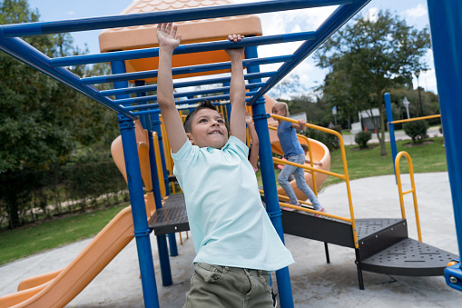 Latin american boy having fun on the monkey bars at the playground looking very happy