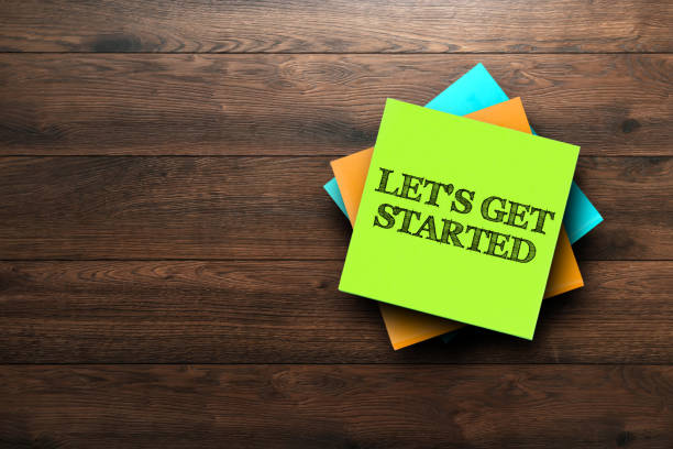 let's get started, the phrase is written on multi-colored stickers, on a brown wooden background. business concept, strategy, plan, planning. - beginnings imagens e fotografias de stock