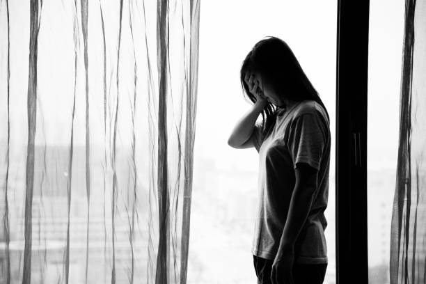 istock Pensive woman standing near the window 956959784