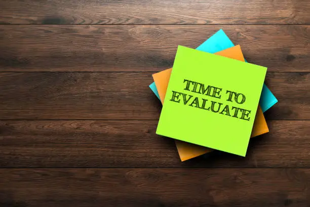 Photo of Time To Evaluate, the phrase is written on multi-colored stickers, on a brown wooden background. Business concept, strategy, plan, planning.