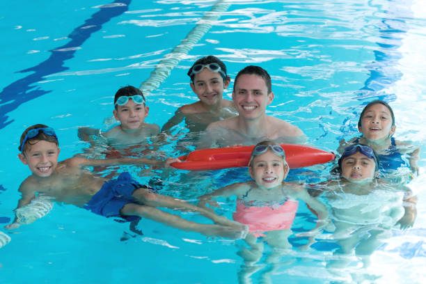 instructeur de natation avec ses élèves dans la piscine tout en regardant caméra très heureux pendant que l’enseignant est titulaire d’un sauvetage bouée - swimming pool child swimming buoy photos et images de collection