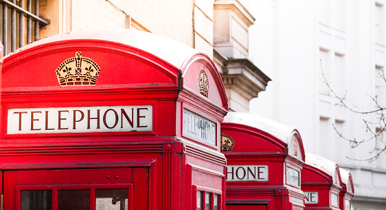 Color image depicting four iconic red British telephone booths in a row in central London, UK. Focus is on the telephone box in the immediate foreground, while the others are slightly defocused in the background. Room for copy space.