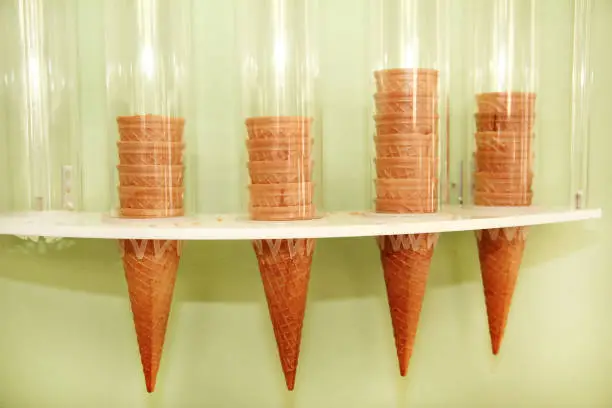 Ice cream waffle cones on dispenser. Ice cream cornets packed in dispenser on the wall of the store. Italian pastry-shop. Sweet, egg product, summer season. Shop of sweets, dessert.