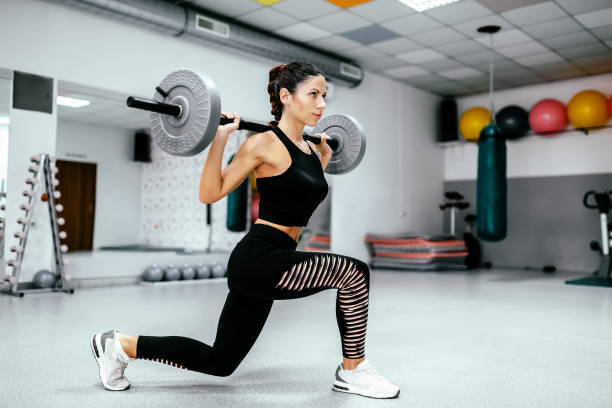 istock Athletic woman doing weighted lunges with barbell on a back. 956982436