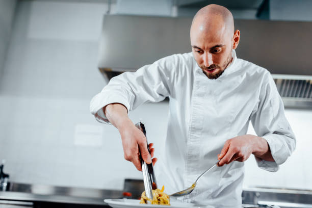 The art of plating Shot of a young cook plating pasta indoors restaurant hotel work tool stock pictures, royalty-free photos & images