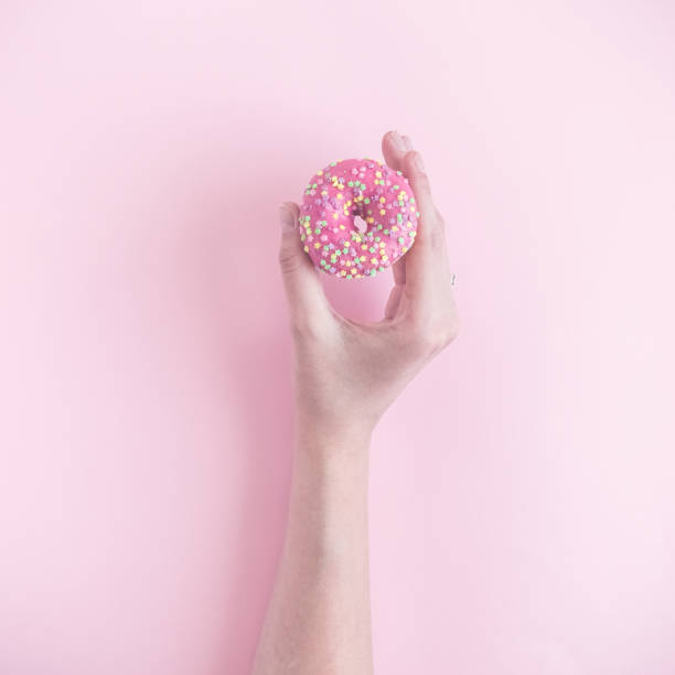 istock Woman hand holding small donut isolated on rose background. 956988916
