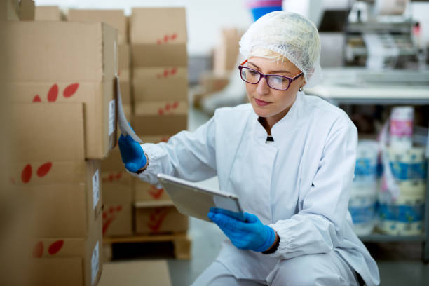 istock Young beautiful focused female worker in sterile cloths using a tablet to check correction of inventory in factory storage room. 956989024