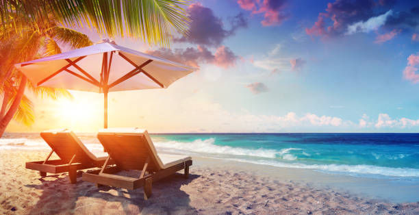 due sedie a sdraio sotto ombrellone nella spiaggia tropicale al tramonto - beach foto e immagini stock