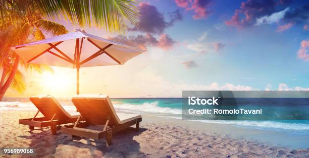 Two Deckchairs Under Parasol In Tropical Beach At Sunset Stock Photo - Download Image Now