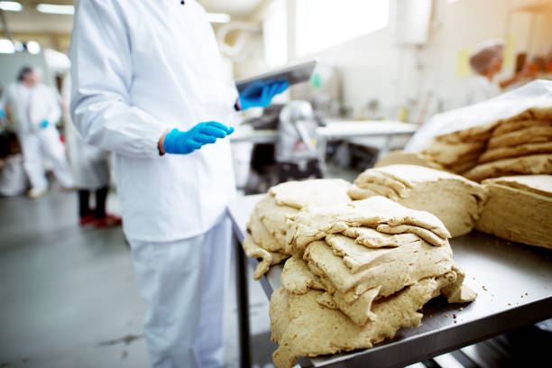 istock Close up dough on a tin desk being inspected by a worker in sterile cloths while holding a tablet in healthy food production line. 956990524