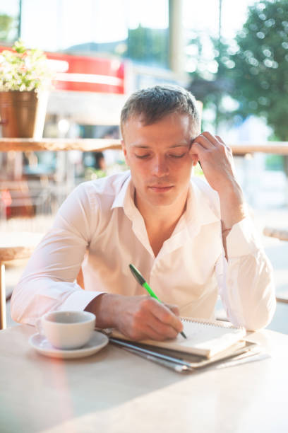 istock Man writing on notebook or planner with smartphone and coffee at outdoor cafe. 956990864