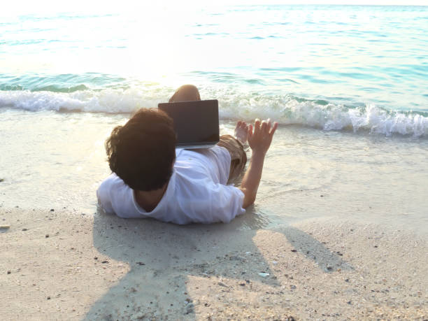 istock Relaxed young Asian man with laptop lying down on the beach. Summer vacations concept. 956994764