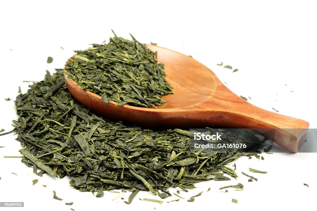 Partially-filled wooden spoon laying on loose green tea Green tea leaves and wooden spoon isolated on white (Shallow dof) Green Tea Stock Photo