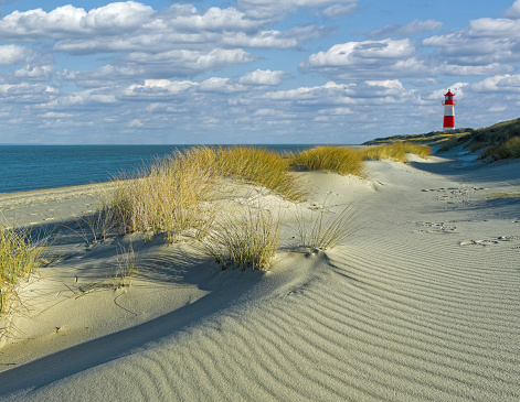 Red and white lighthouse with curvy sand dunes at the beach of island Sylt, Germany