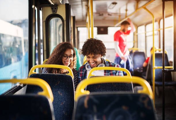 istock Young happy gorgeous couple is sitting together in a bus and smiling while looking at something hidden behind the bus seat. 957002016
