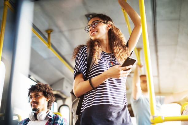 giovane adorabile donna gioiosa è in piedi sull'autobus usando il telefono e sorridendo. - pendolare foto e immagini stock