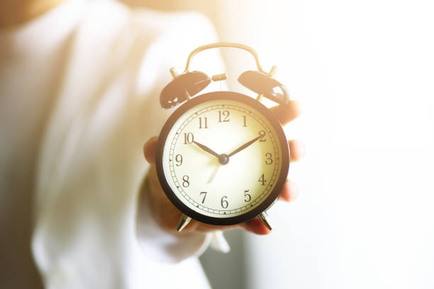 istock Classic black alarm clock in a hand. Sunny morning light. Copy space 957009538